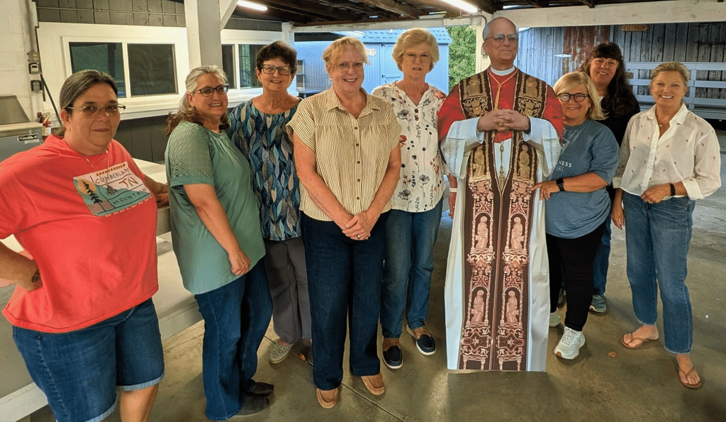 Eight women from Holy Spirit Catholic Church standing with a life-size cardboard cutout of Pope Leo XIV