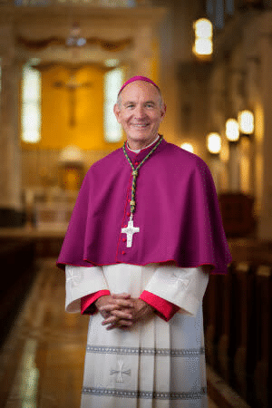 Bishop Mark Beckman standing in a church, wearing a violet cape and a pectoral cross
